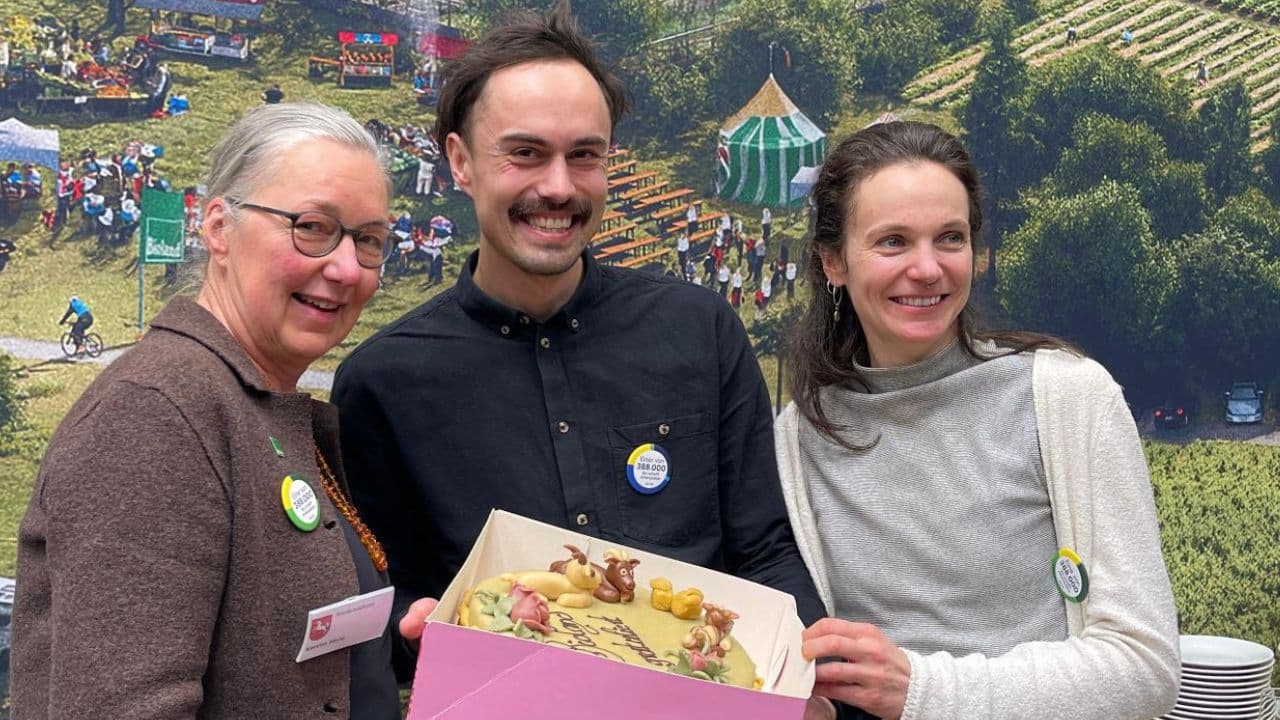 Drei lächelnde Personen halten eine verzierte Torte in einer Schachtel.